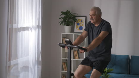 home-training-on-stationary-bicycle-middle-aged-man-is-spinning-pedals-in-living-room-healthy-lifestyle-and-keeping-fit